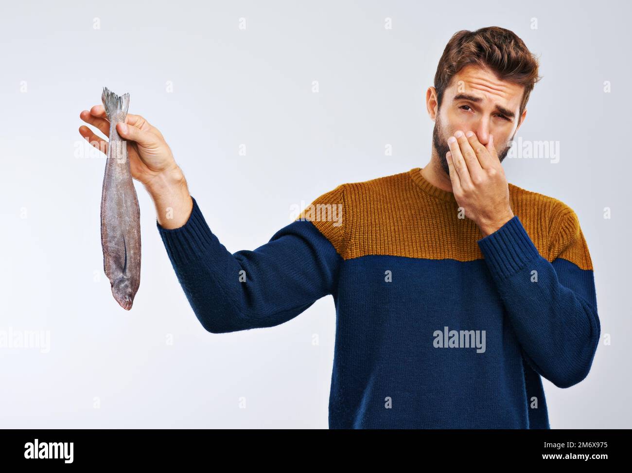 A fish by any other name would smell as gross. Studio shot of a man showing disgust while holding a smelly fish. Stock Photo