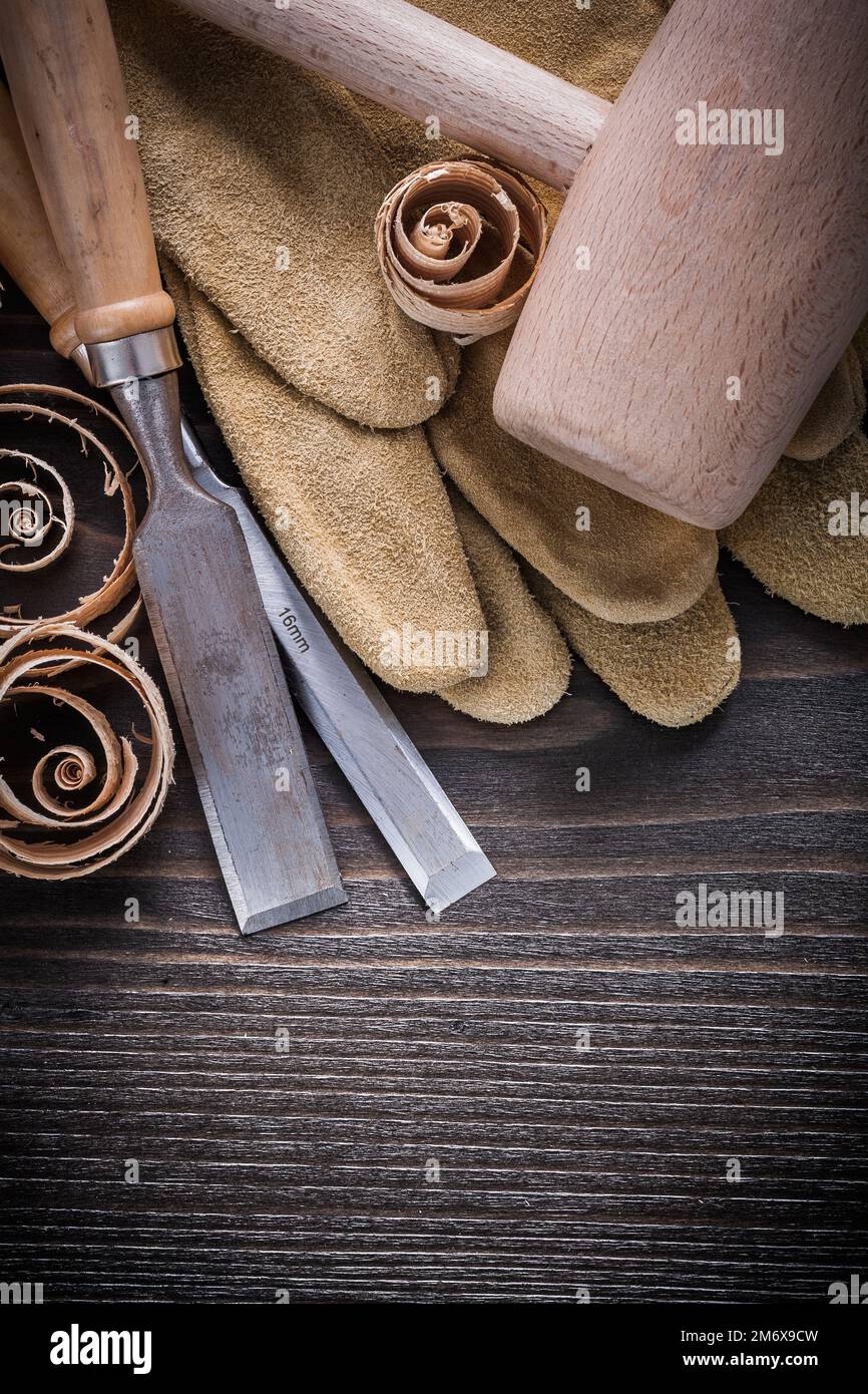 Brown leather gloves flat chisels wooden hammer and shavings on vintage wood board construction concept. Stock Photo