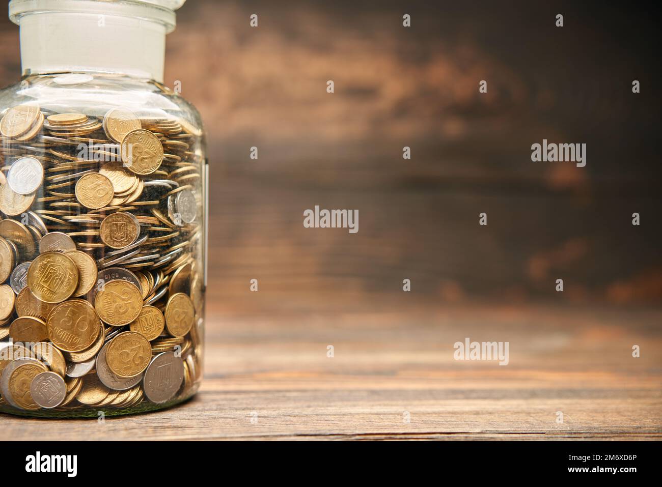 Glass jar filled of golden coins with  copy space for text on wooden background. Stock Photo