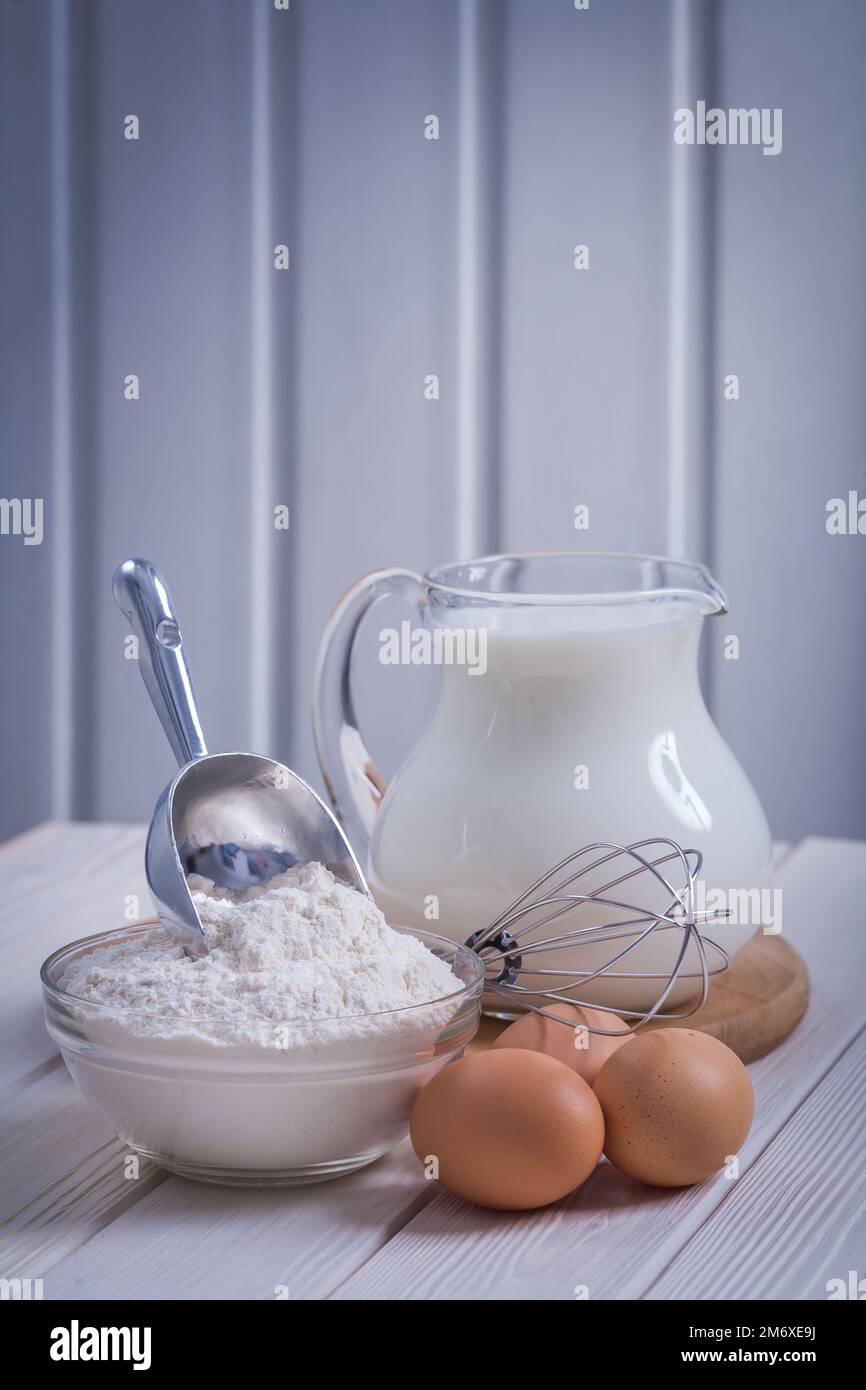 https://c8.alamy.com/comp/2M6XE9J/flour-in-bowl-scoop-egs-corolla-jug-with-milk-on-white-painted-old-wooden-board-food-and-drink-concept-2M6XE9J.jpg