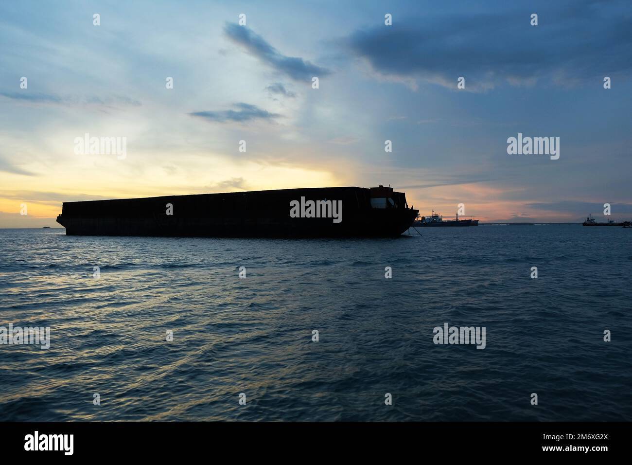 The dark silhouette of a barge in the sea against a light background of the rising sun. Sky view with boat shadow Stock Photo