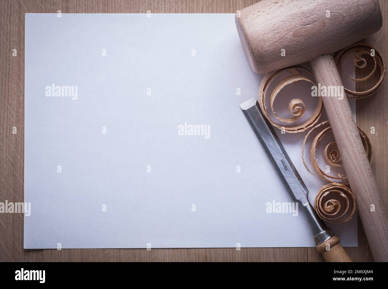 Curled shavings firmer chisels wooden mallet and blank sheet of paper on wood board copy space image construction concept. Stock Photo