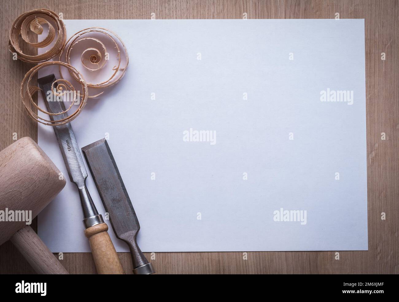 Curled wooden shavings firmer chisels lump hammer and blank sheet of paper on wood board copyspace image construction concept. Stock Photo