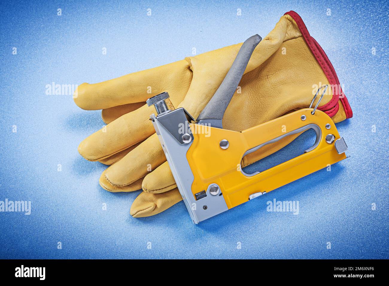 Leather safety gloves stapler gun on blue background construction concept. Stock Photo