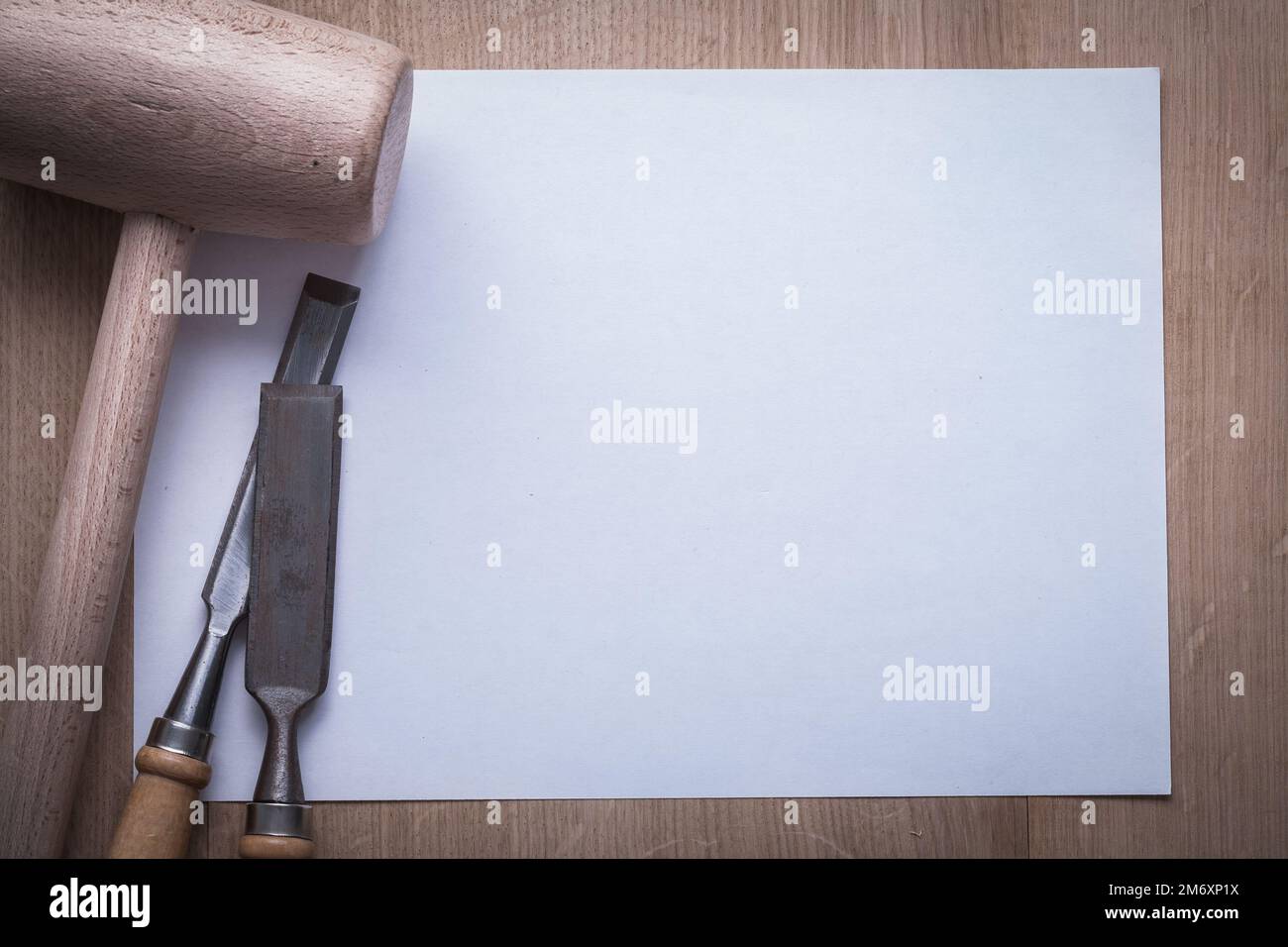 Metal firmer chisels lump hammer and blank sheet of paper on wooden board copy space construction concept. Stock Photo