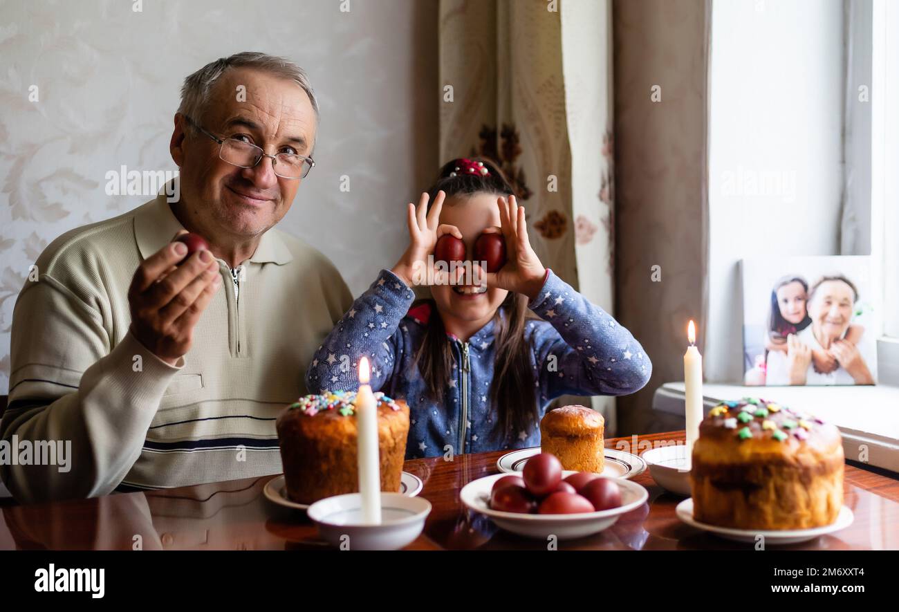 happy grandfather and granddaughter hold easter eggs in hand, folk game