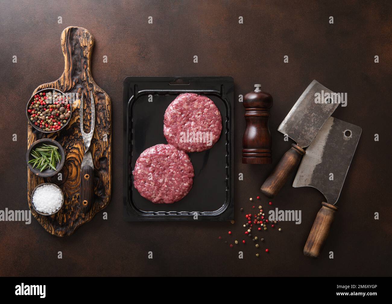 Raw beef burgers sealed in vacuum tray with cleavers on dark kitchen