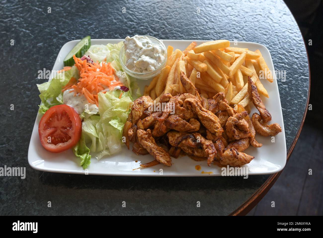 Fried chicken dish with fries, salad and cream dip on a square plate served on a black table in a fast food restaurant, selected focus, narrow depth o Stock Photo
