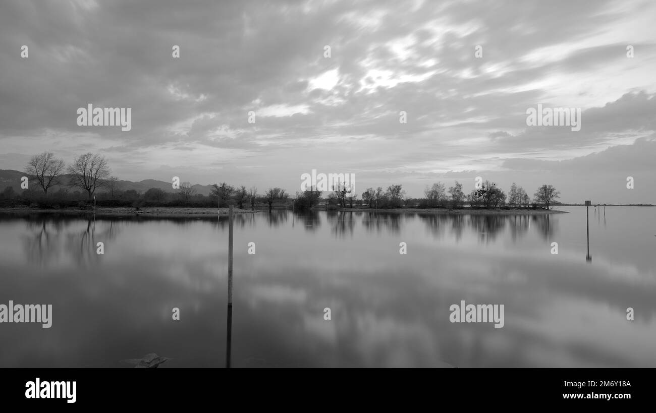 Long time exposure of Lake Constance at sunset with passing clouds and reflections in water in black and white Stock Photo