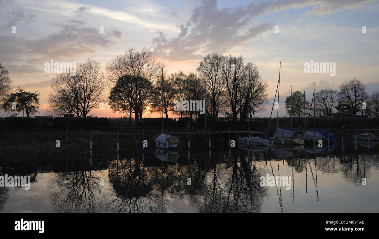 Reflection of trees in water in sunset at small harbor on Lake Constance in Hard near Bregenz with Slide from swimming pool in background Stock Photo