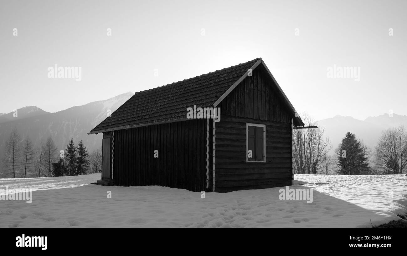 Wooden hut with gable roof in the snow that casts a large shadow in black and white in Austria Stock Photo