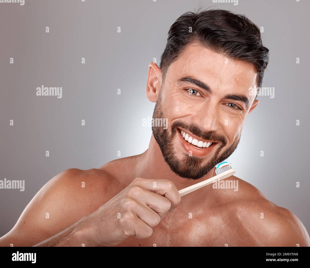 Portrait, man and brushing teeth with smile, dental hygiene and on grey studio background. Gum care, male and toothbrush for healthcare, toothpaste Stock Photo