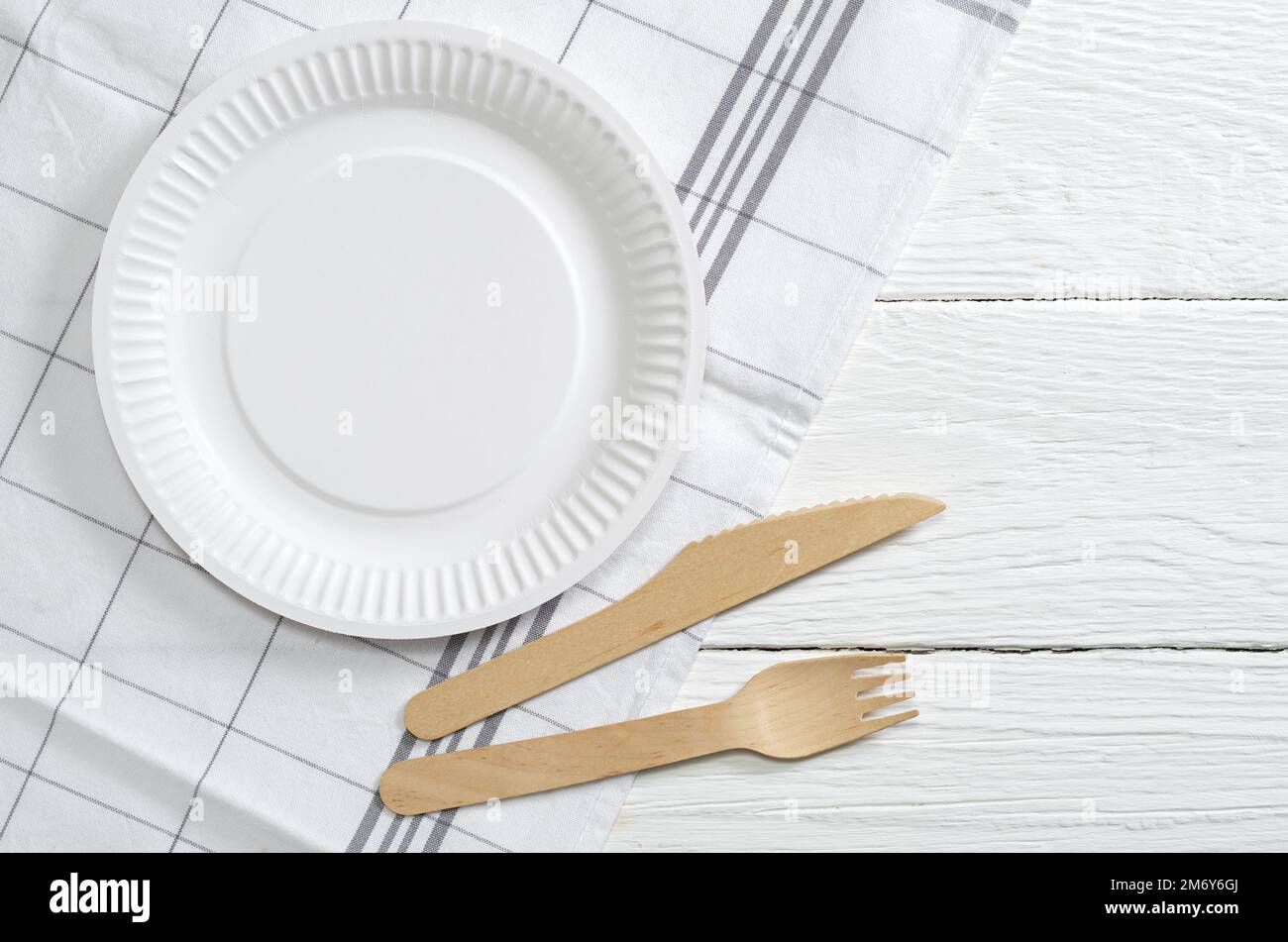 Paper plate, wooden fork and knife on white table, top view. Disposable