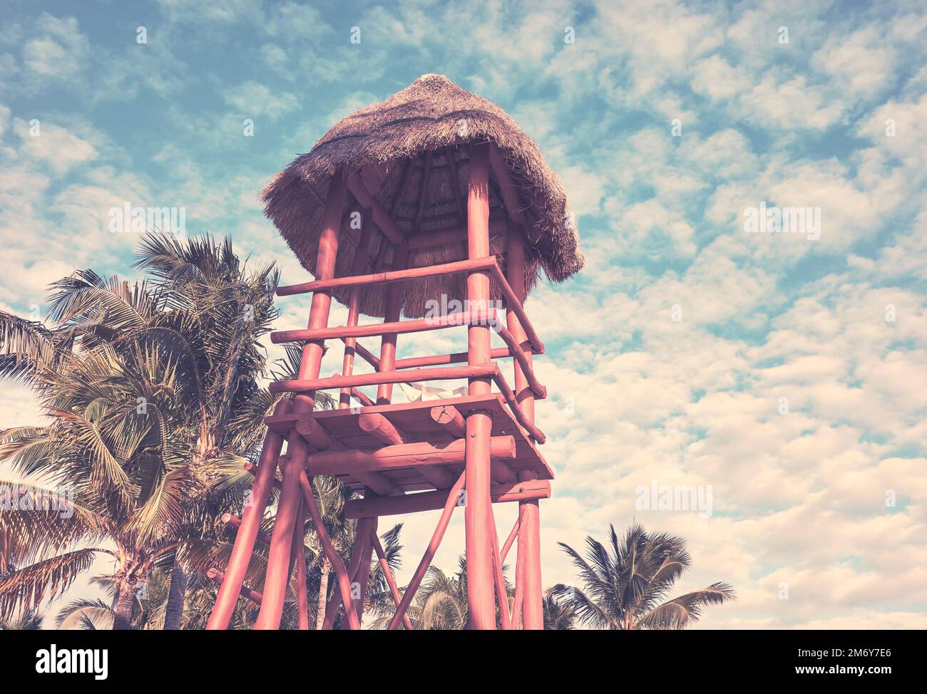Wooden lifeguard tower on a Caribbean beach against the sky with coconut palm trees in background, color toning applied. Stock Photo