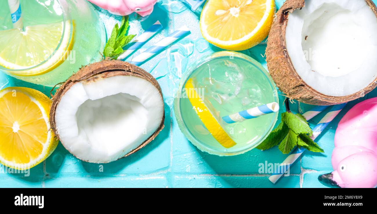 Bright sunny summer vacation. Lemonade drink on wet blue pool tiles background, with beach holiday accessories, flamingo lifebuoys, lemons, coconuts, Stock Photo