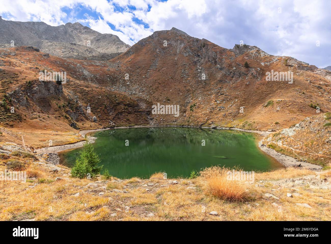 Emerald water of Lake Loie (Lago di Loie) surrounded by granite alpine rocks with autumn withered yellow grass in Parco Nazionale Gran Paradiso Stock Photo