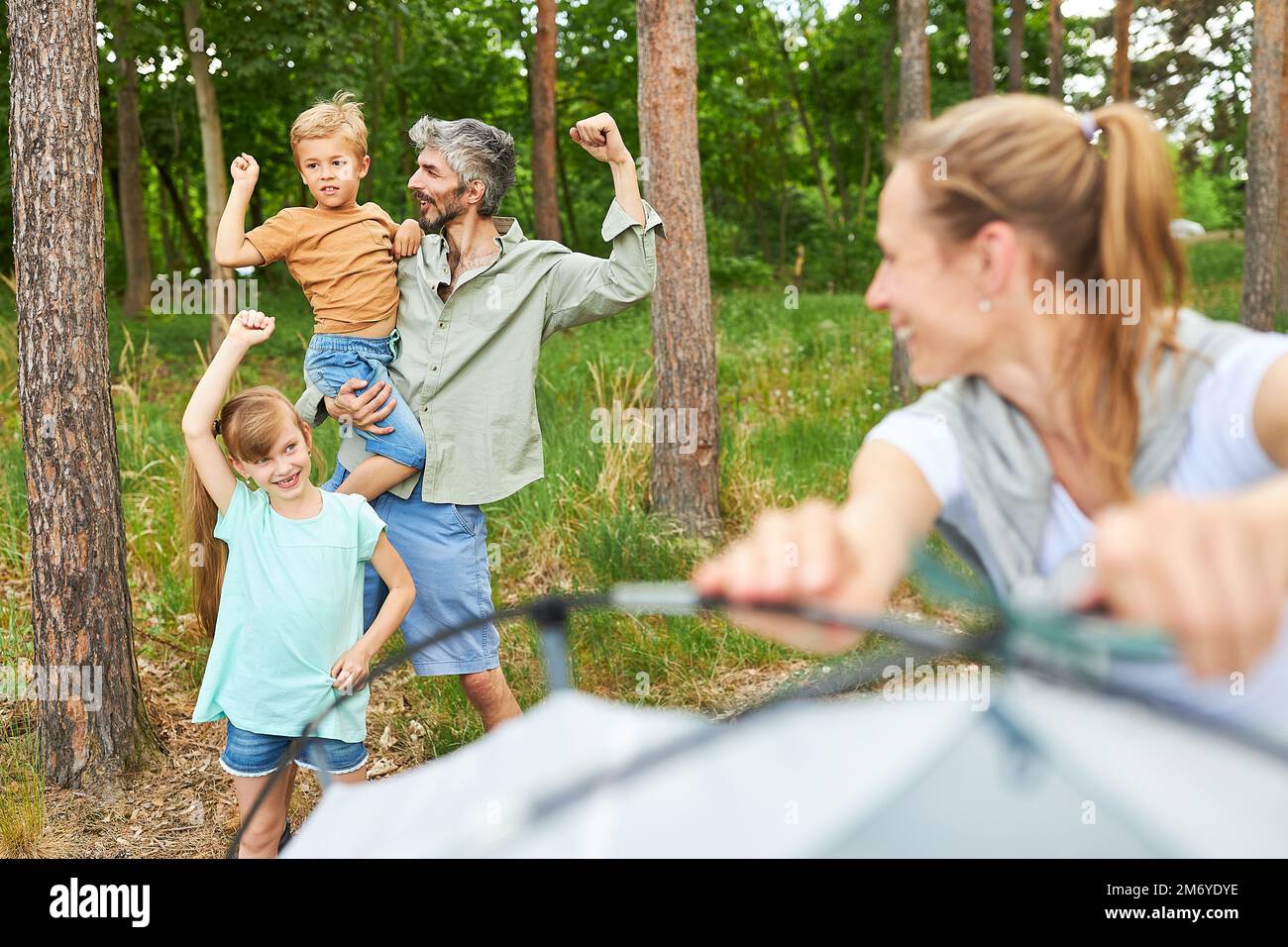 Woman setting up tent and looking at family cheering while camping together during summer vacation Stock Photo