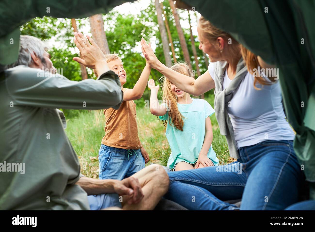 Happy siblings giving high-five to parents sitting in tent during summer vacation Stock Photo