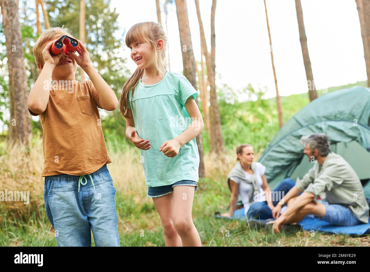 Boy looking through binoculars standing by happy sister while camping with family Stock Photo