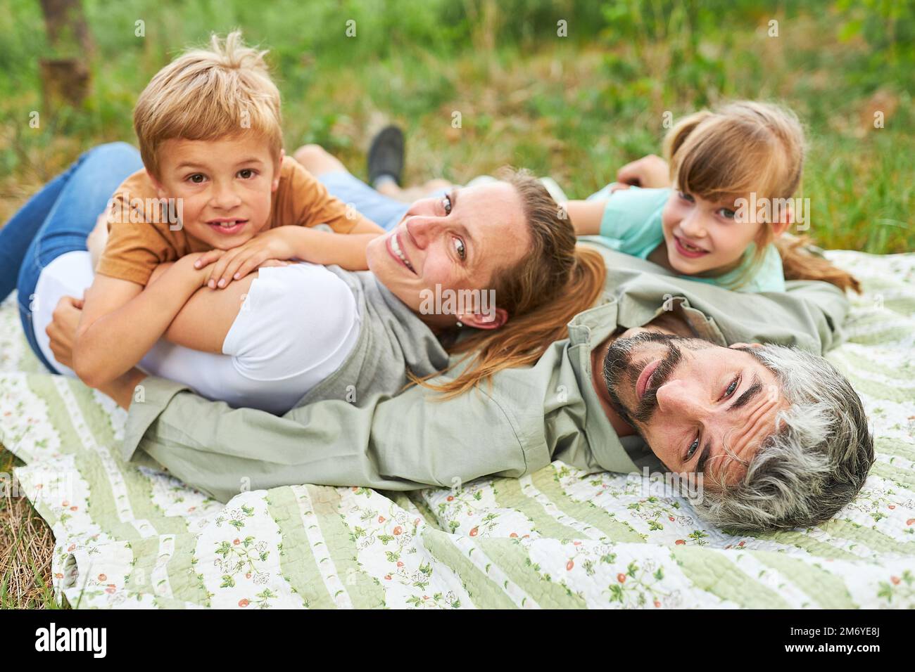 Portrait of smiling family lying on blanket at campsite during summer ...
