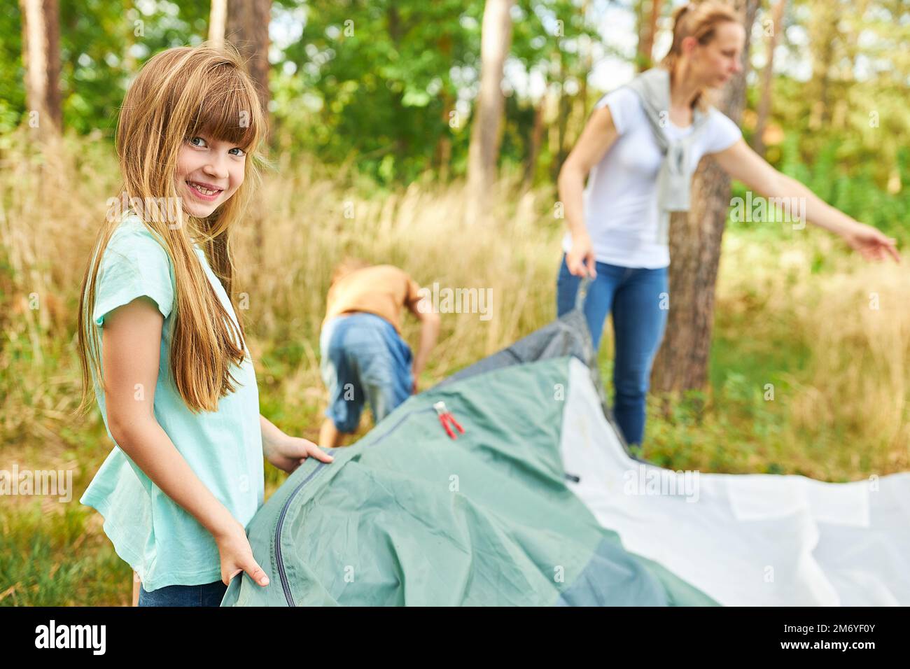 Portrait of smiling girl setting up tent for camping with family in forest during vacation Stock Photo