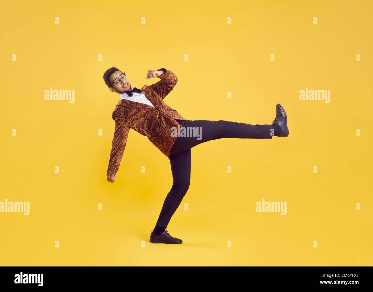 Cheerful eccentric and funny young dark-skinned man in leopard jacket isolated on yellow background. Stock Photo
