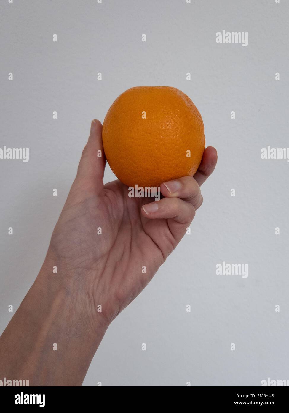 A woman's hand holding a ripe orange against a white background. Ready-to-eat fruit Stock Photo