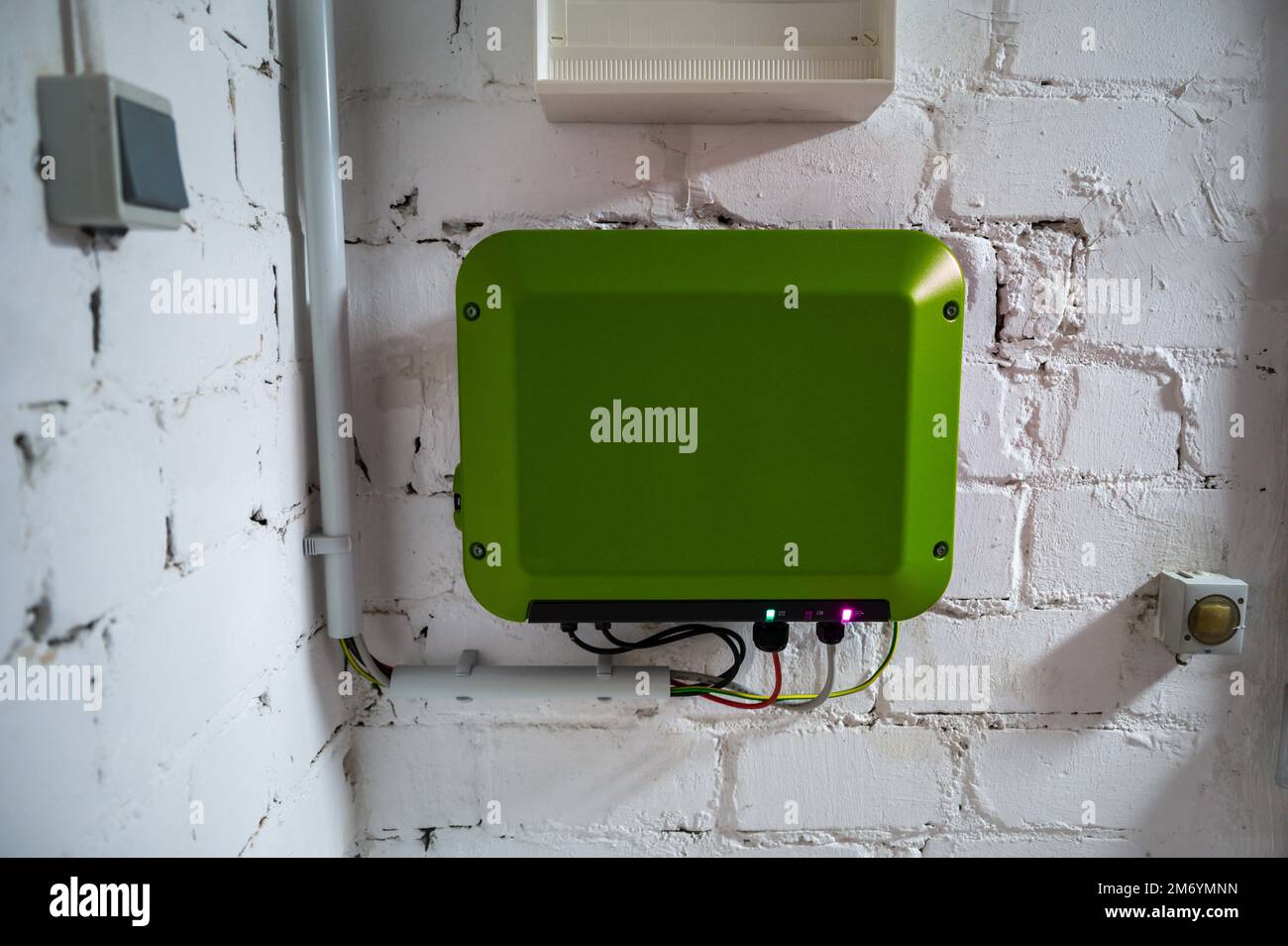 Green inverter of a photovoltaic system mounted on a white basement wall Stock Photo