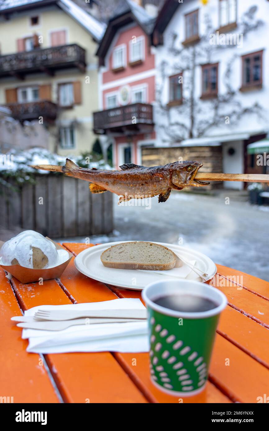 eating skewered fish with gluhwein in Hallstatt at the christmas market on main square . Stock Photo