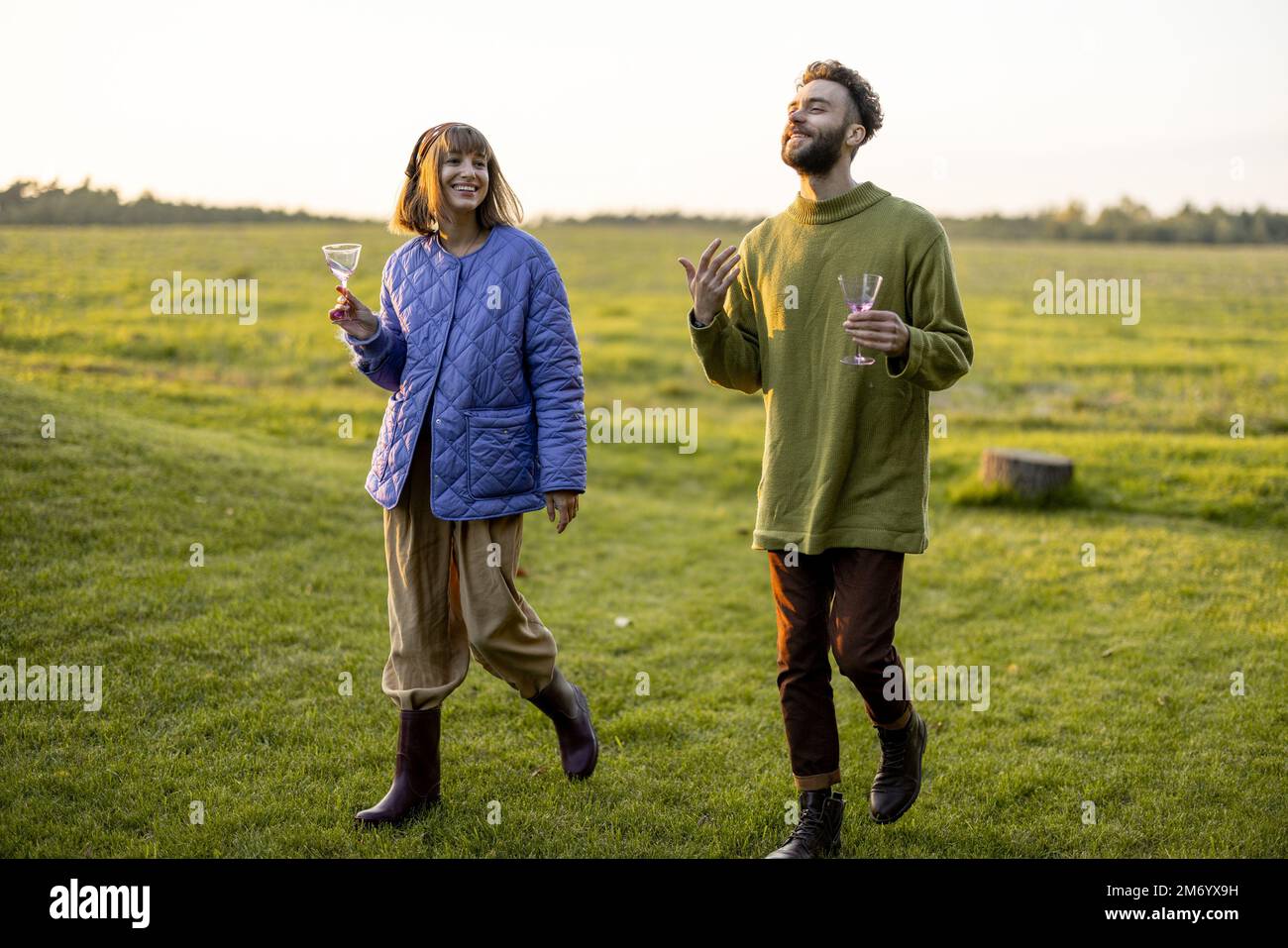 Couple hang out together, walking on green field on sunset Stock Photo