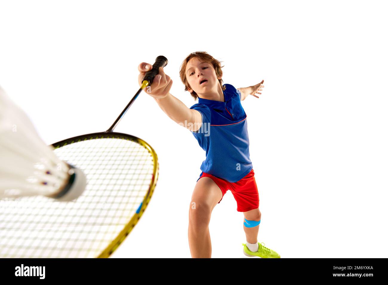 Portrait of teen boy in uniform playing badminton, hitting shuttlecock with racket isolated over