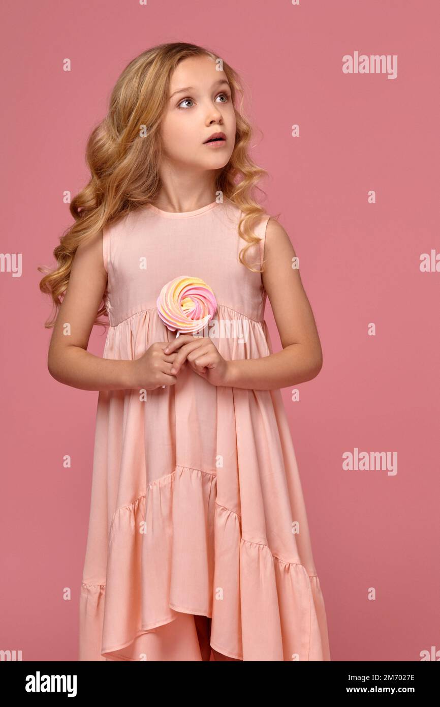 Little girl with a blond curly hair, in a pink dress is posing with a ...