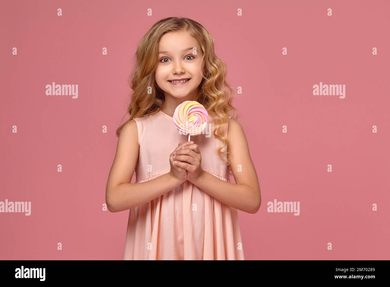 Little girl with a blond curly hair, in a pink dress is posing with a ...