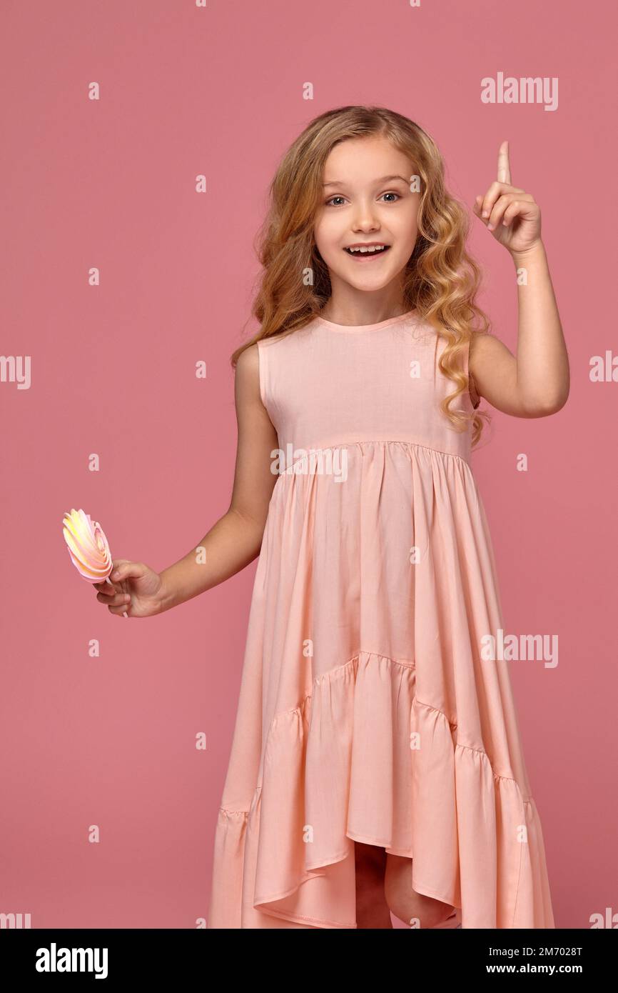 Little girl with a blond curly hair, in a pink dress is posing with a ...