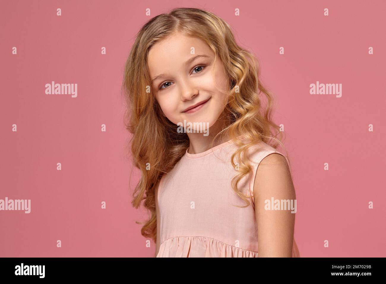 Little girl with a blond curly hair, in a pink dress is posing for the ...