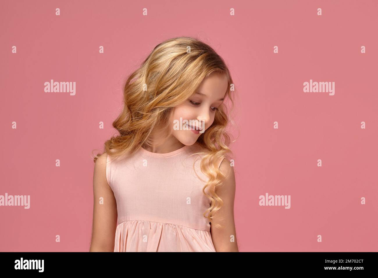 Little girl with a blond curly hair, in a pink dress is posing for the
