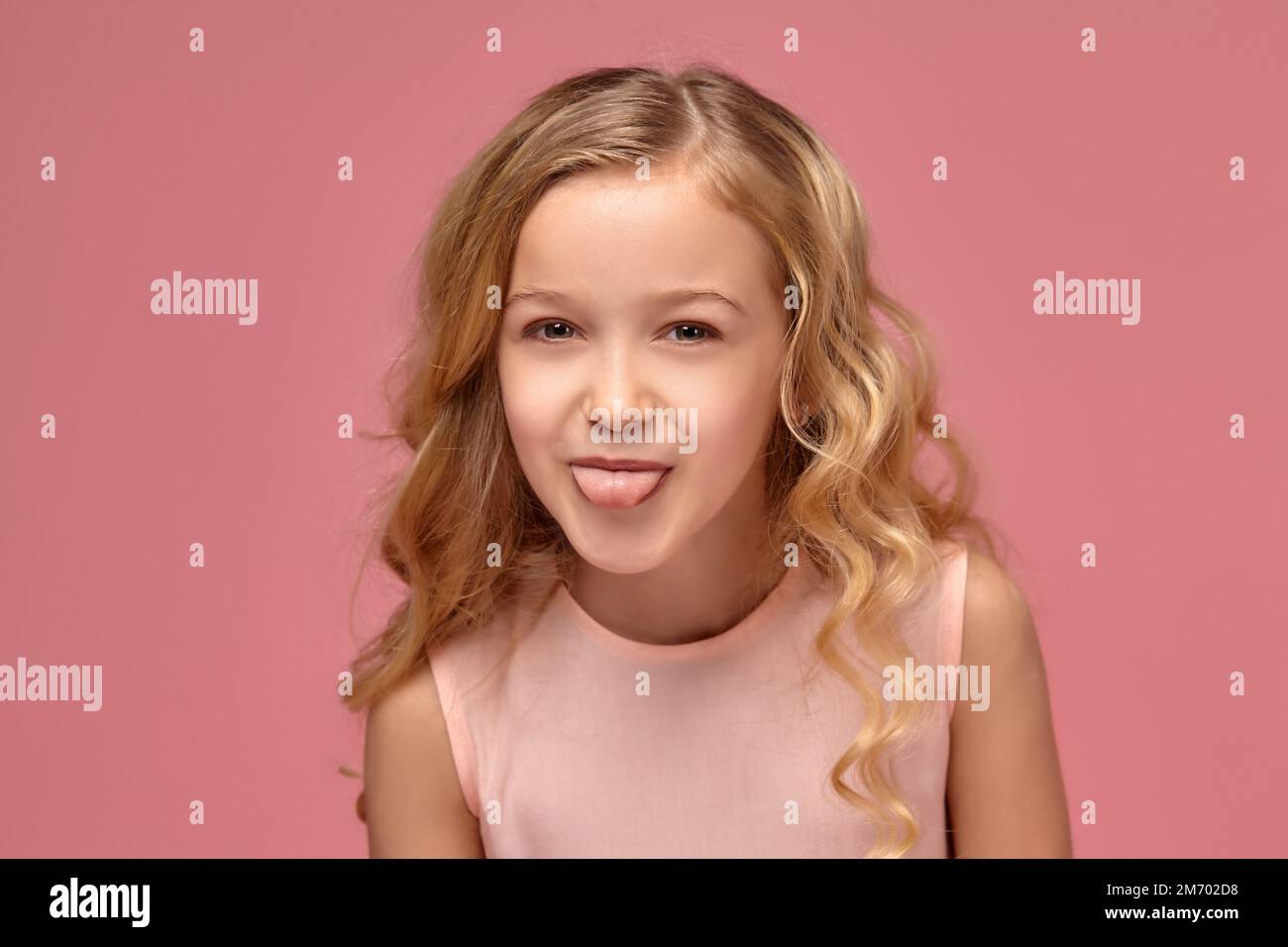 Little girl with a blond curly hair, in a pink dress is posing for the ...