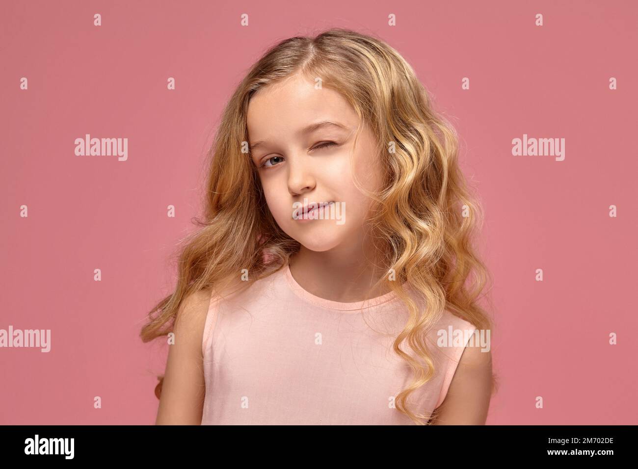 Little girl with a blond curly hair, in a pink dress is posing for the ...