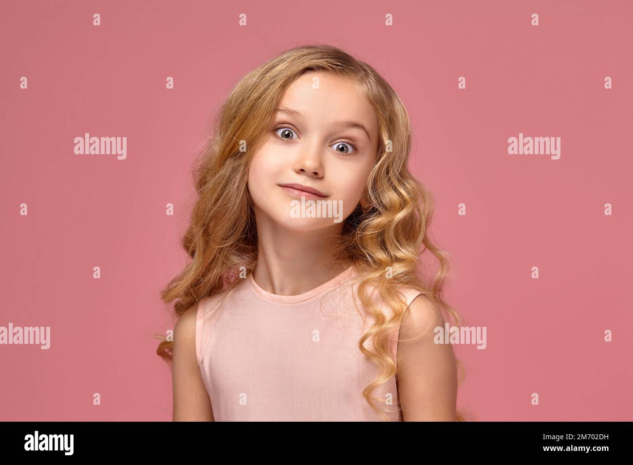Little girl with a blond curly hair, in a pink dress is posing for the ...