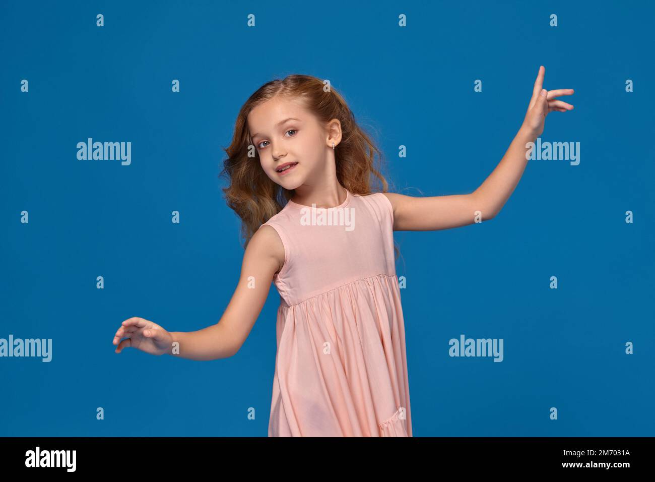 Fashionable little girl in a pink dress is posing on a blue background ...