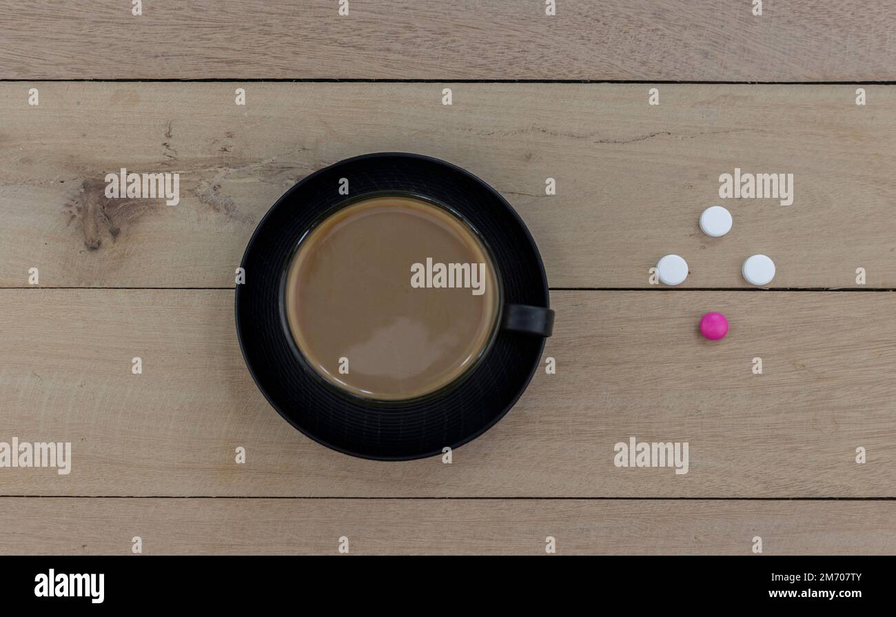 A cup of coffee on a wooden table next to painkillers and antibiotics as a symbol of the