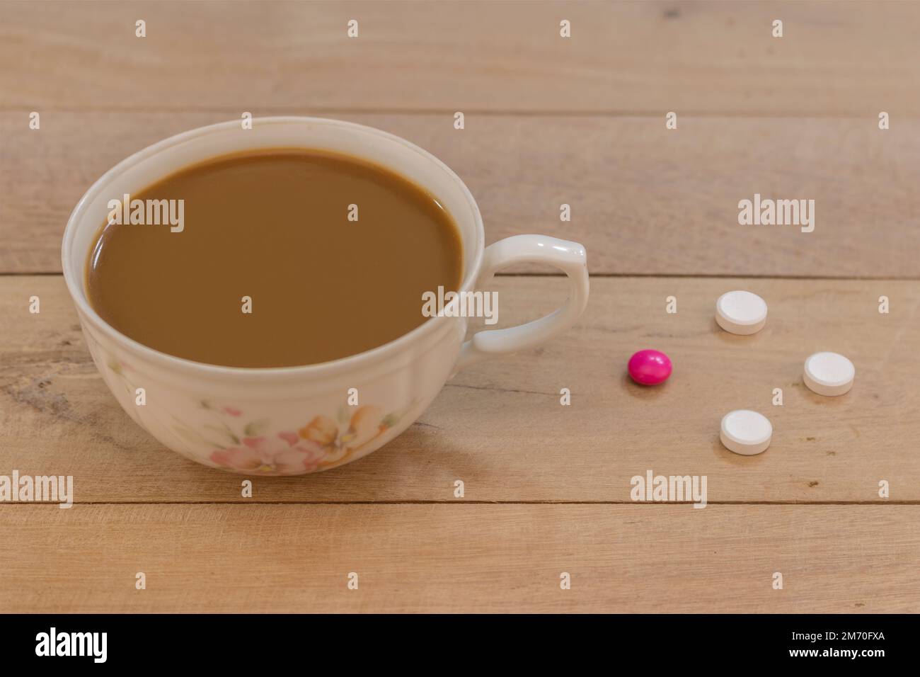 A cup of coffee on a wooden table next to painkillers and antibiotics