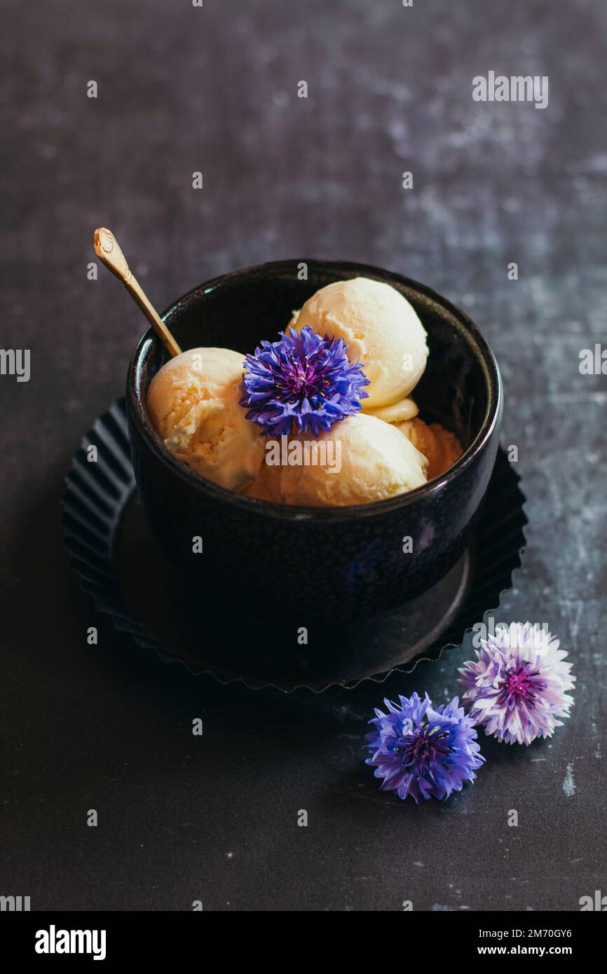 vanilla ice cream scoops with edible flowers in a black bowl on a dark ...