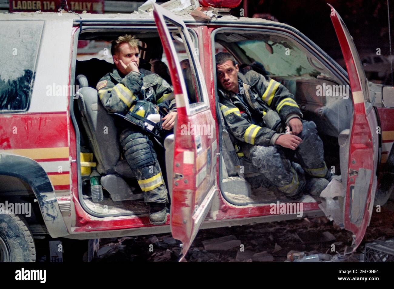 Two exhausted New York City firefighters rest inside a destroyed FDNY battalion chief's vehicle as they wait for further orders on West Drive, just so Stock Photo