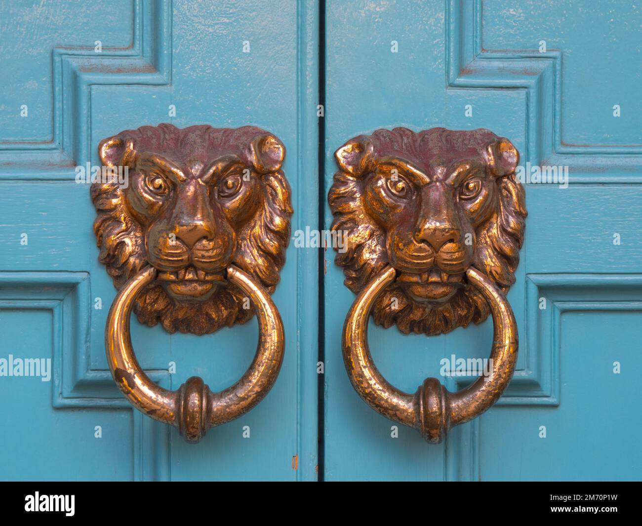 Traditional door knockers on a wooden blue door, brass made, showing the face of a lion. Typical