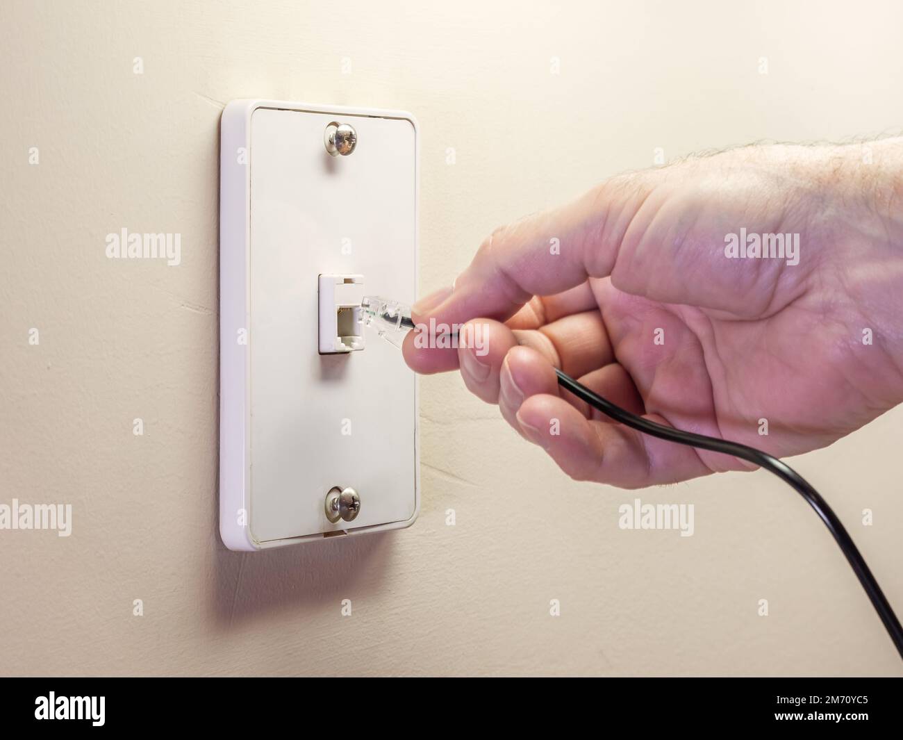Male electrician plugging in landline telephone cord into wall mounted jack plate. Stock Photo