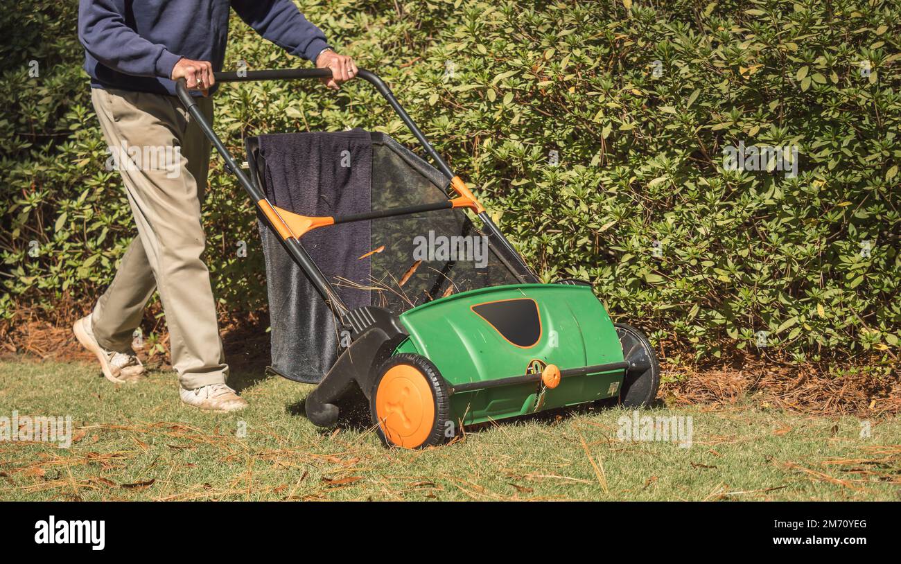 Man using manual push lawn sweeper to remove fall leaves from