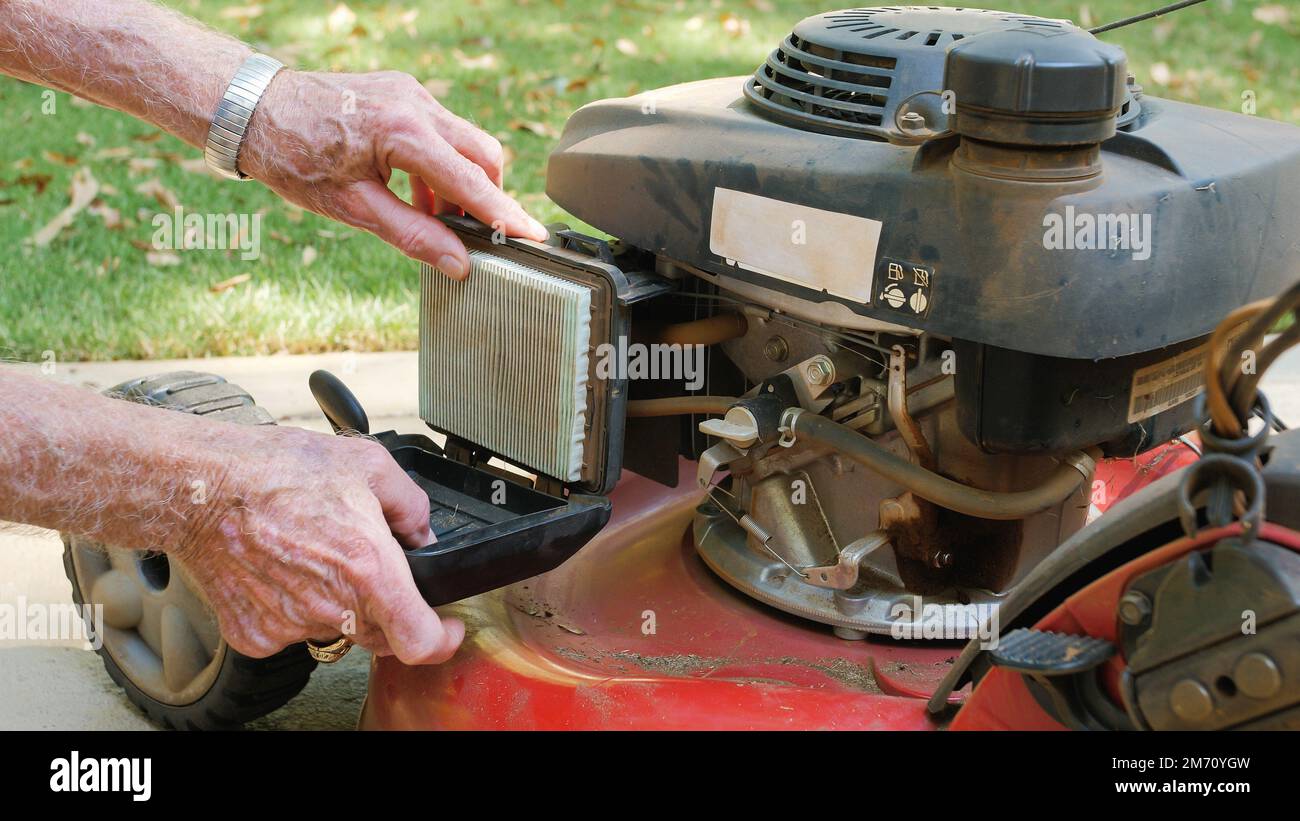 Male landscaper replacing air filter on gas powered lawn mower. Checking air cleaner filter for proper maintenance. Stock Photo
