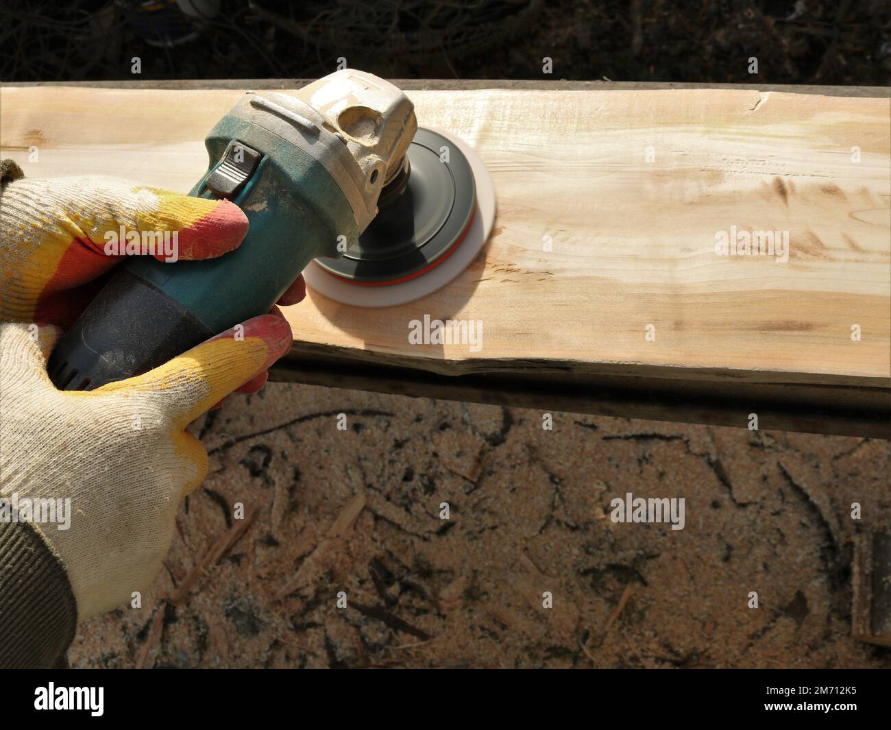 carpenter's hands in protective textile gloves hold a grinder with a