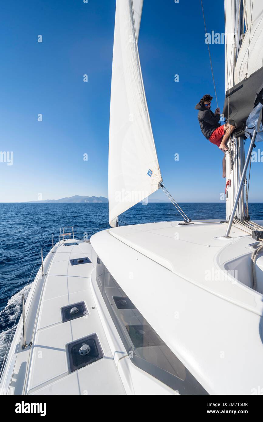 Sailor adjusts the sails on the mast, sailing catamaran sailing, South Aegean Sea, Greece Stock Photo